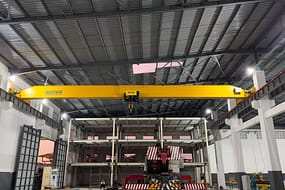  带有 DGCRANE 品牌的 FEM 标准黄色桥式起重机，位于大型工业建筑区域，下方有金属结构和重型机械